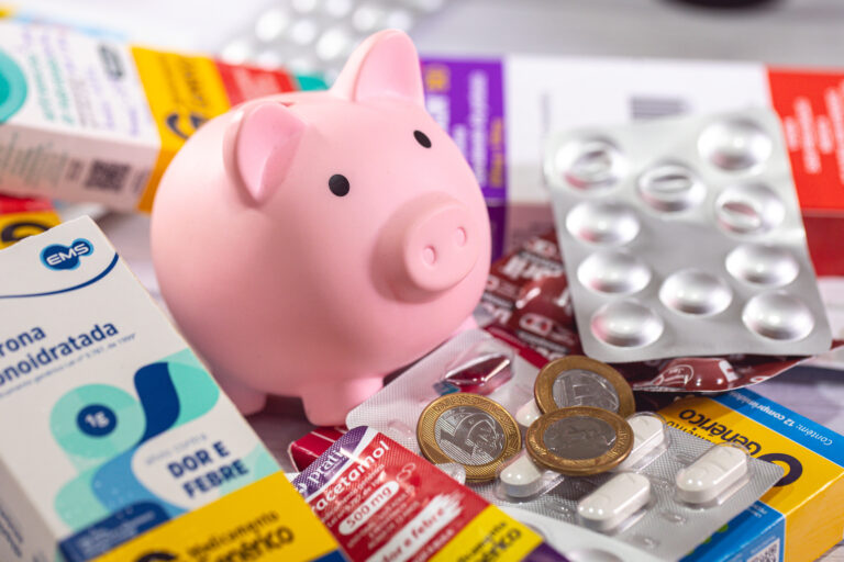 Symbolbild: Ein Sparschwein steht zwischen Medikamenten, Blisterpackungen und Münzen.