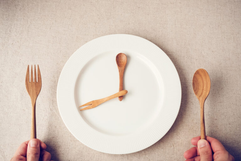 Symbolbild: Ein weißer leerer Teller mit Holzlöffel und Holzgabel, daneben weiteres Holzbesteckt.
