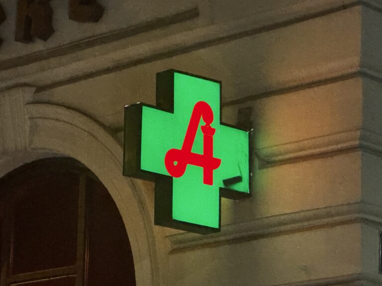 Ein grün leuchtendes Apothekenkreuz mit Apotheker A deutet auf den Nachtdienst hin.