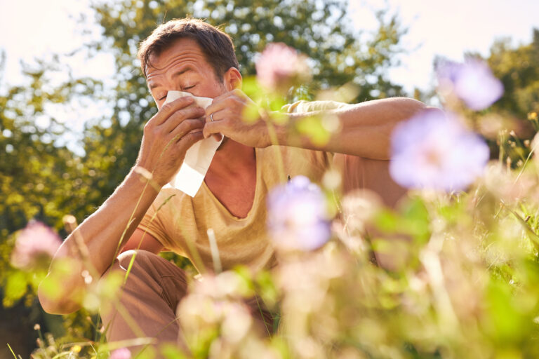 Symbolbild: Mann sitzt in Blumenwiese und schnäuzt sich.