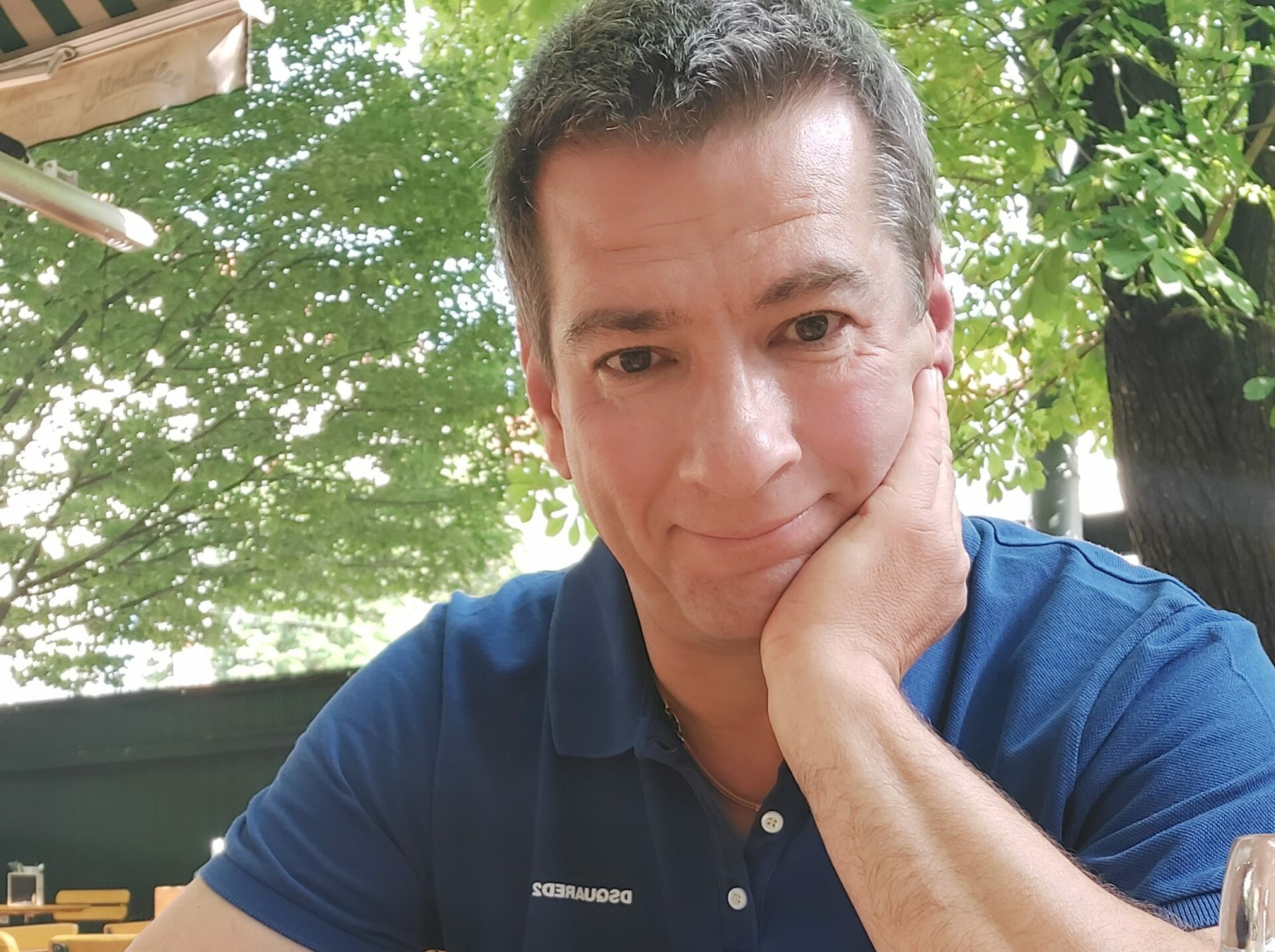 Rhehor stützt sein Kinn in die linke Hand und lächelt in die Kamera.