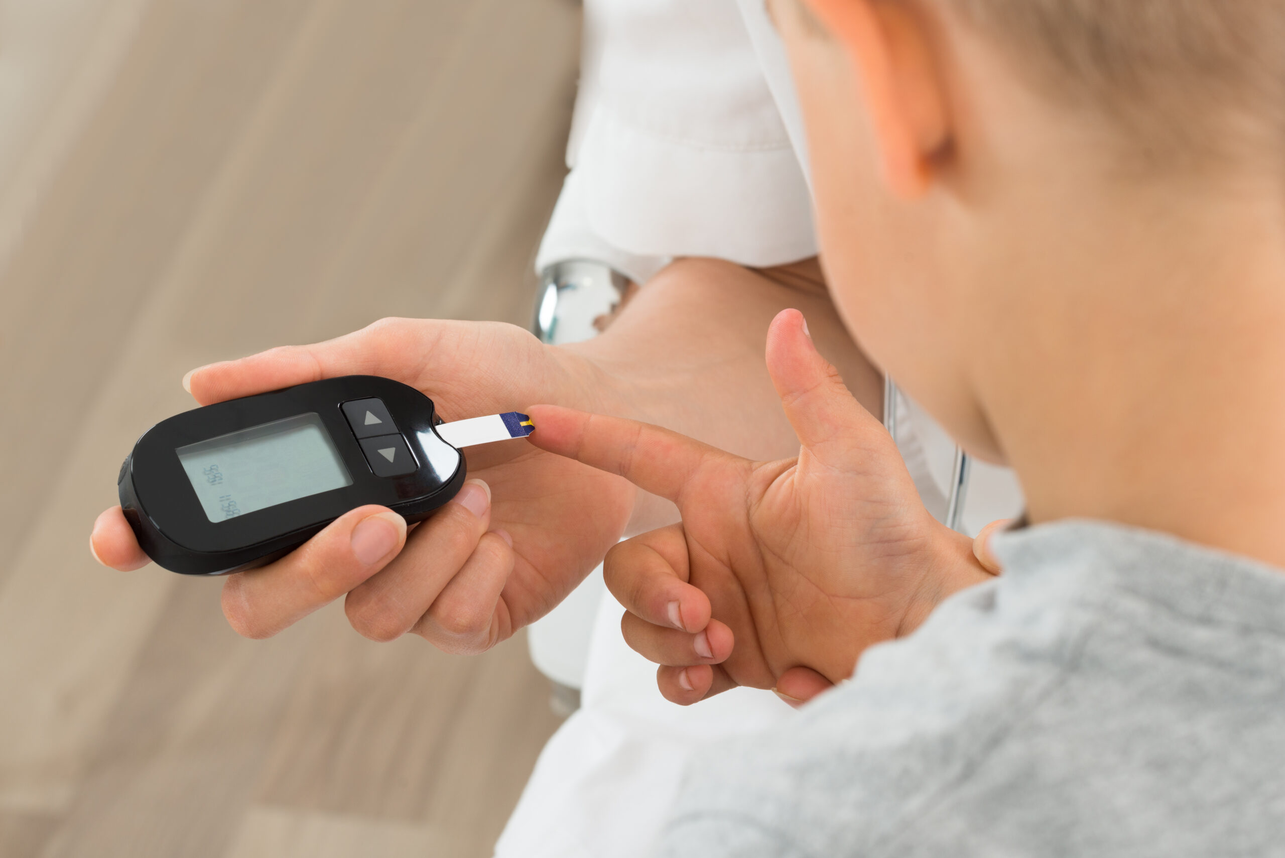 Bube im Kindergartenalter hält seinen Finger an den Messstreifen eines Blutzucker-Testgerätes. Dieses wird von einer erwachsenen Person gehalten.