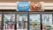 Hinter den geschlossenen Glastüren einer Supermarkt Kühlvitrine stehen viele Schachteln unterschiedlicher Fertigpizzen.
