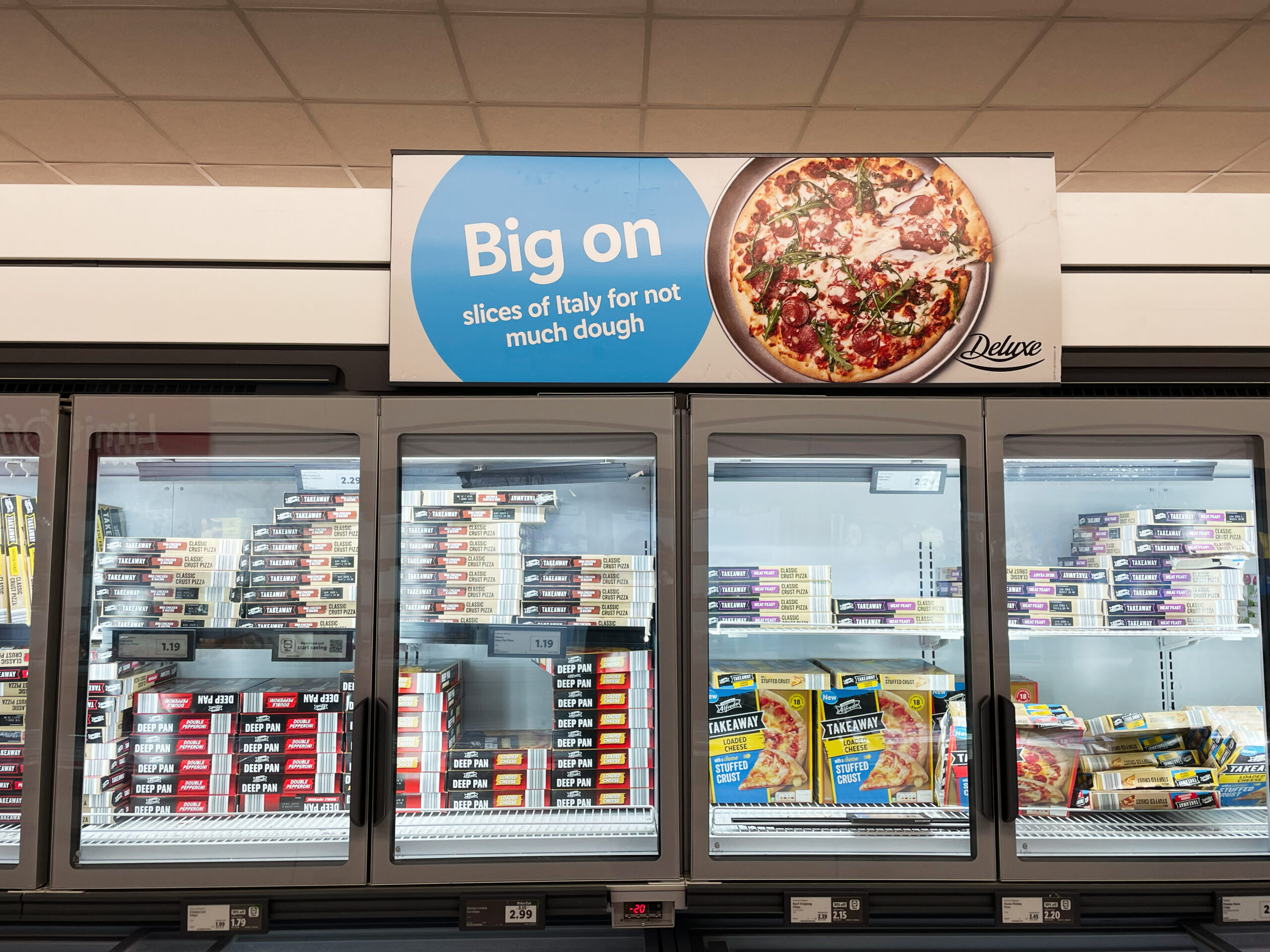 Hinter den geschlossenen Glastüren einer Supermarkt Kühlvitrine stehen viele Schachteln unterschiedlicher Fertigpizzen.