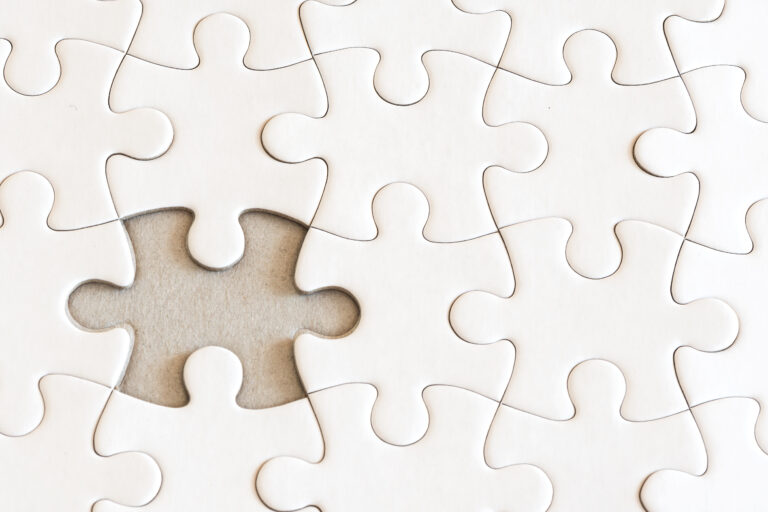 Puzzle aus lauter weißen Teilen. Ein Teilchen fehlt in der Mitte.