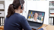 Frau sitzt mit headset vor dem Laptop. Am Bildschirm ist eine Ärztin zusehen, die ebenfalls ein Headset trägt.
