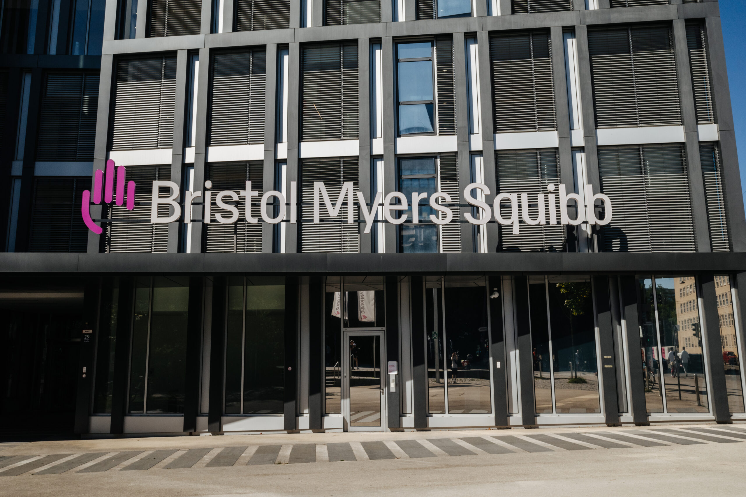 Auf einem Bürogebäude mit moderner grauer Fassade steht über dem Eingang der Schriftzug Bristol Myers Squibb.