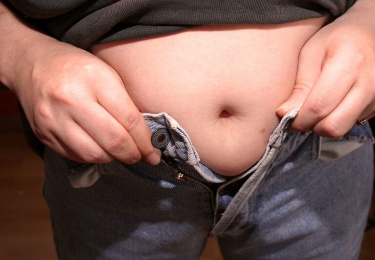 Mann versucht seine Hose zuzumachen, aber der Bauch hängt dazwischen.