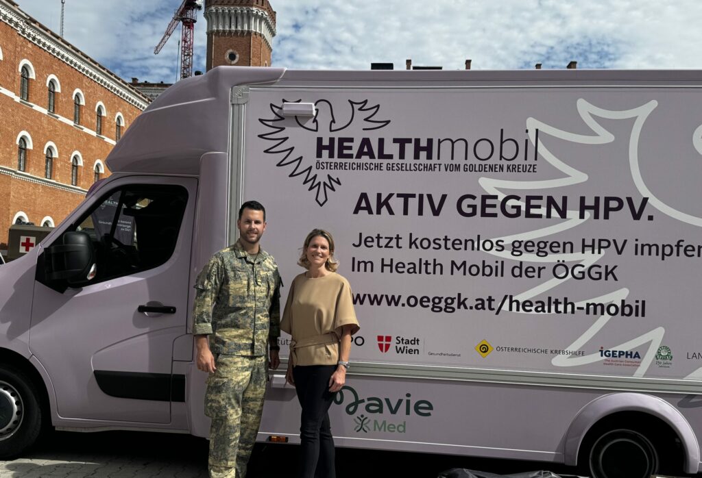 Major Marcel Taschwer und Erika Sander berichten über die Impfaktion in der Rossauer Kaserne. Beide stehen vor dem mobilen Impfbus. Taschwer in Militäruniform und Sander in einem beiden Oberteil mit schwarzer Hose.