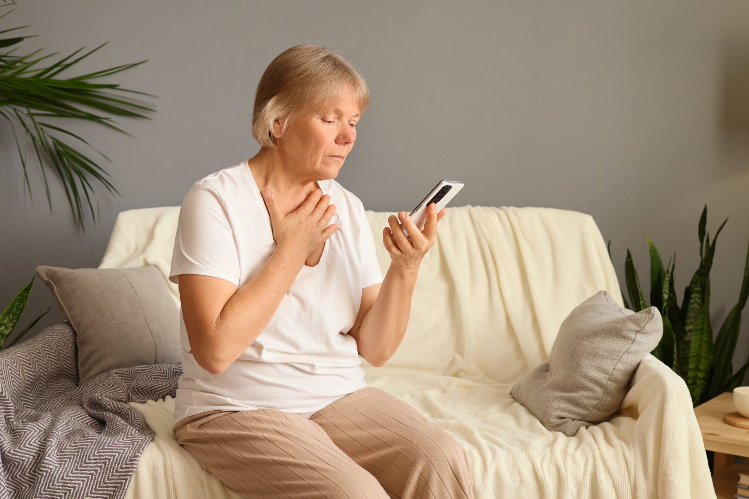 Ältere Frau hält das Handy in der Hand und greift sich mit der anderen an die Brust.