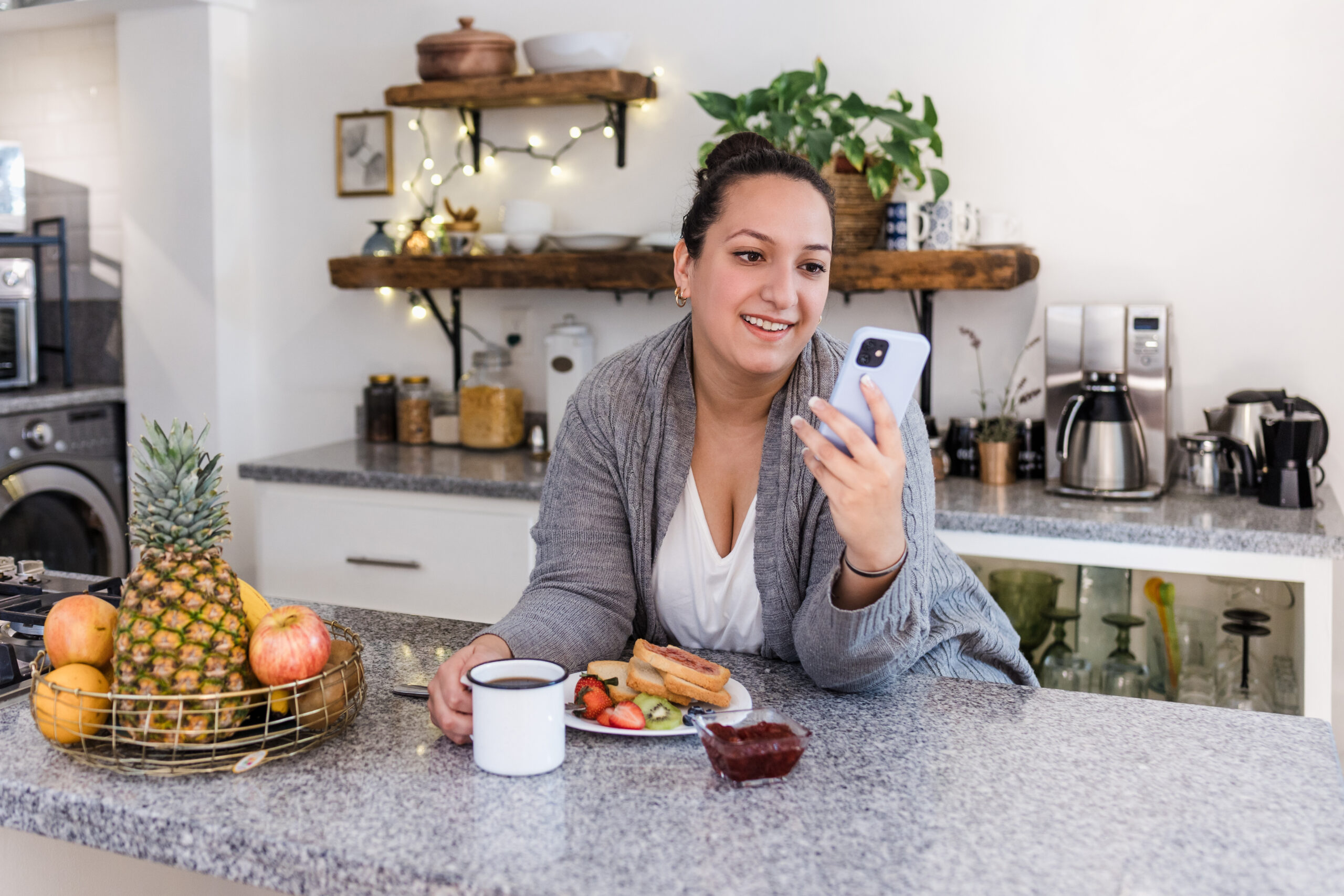 Füllige Frau Mitte 40 lehnt am Küchentresen und blickt auf ihr Handy.