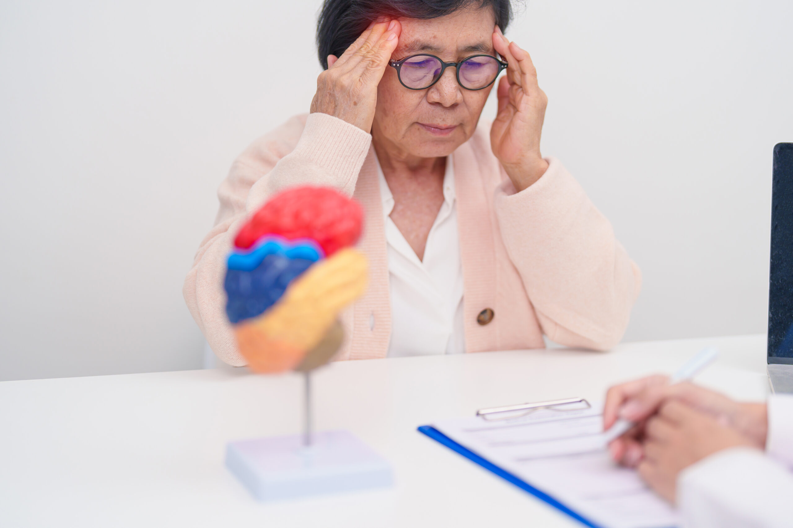 Älter Frau sitz beim arzt und greift sich an die schläfen.