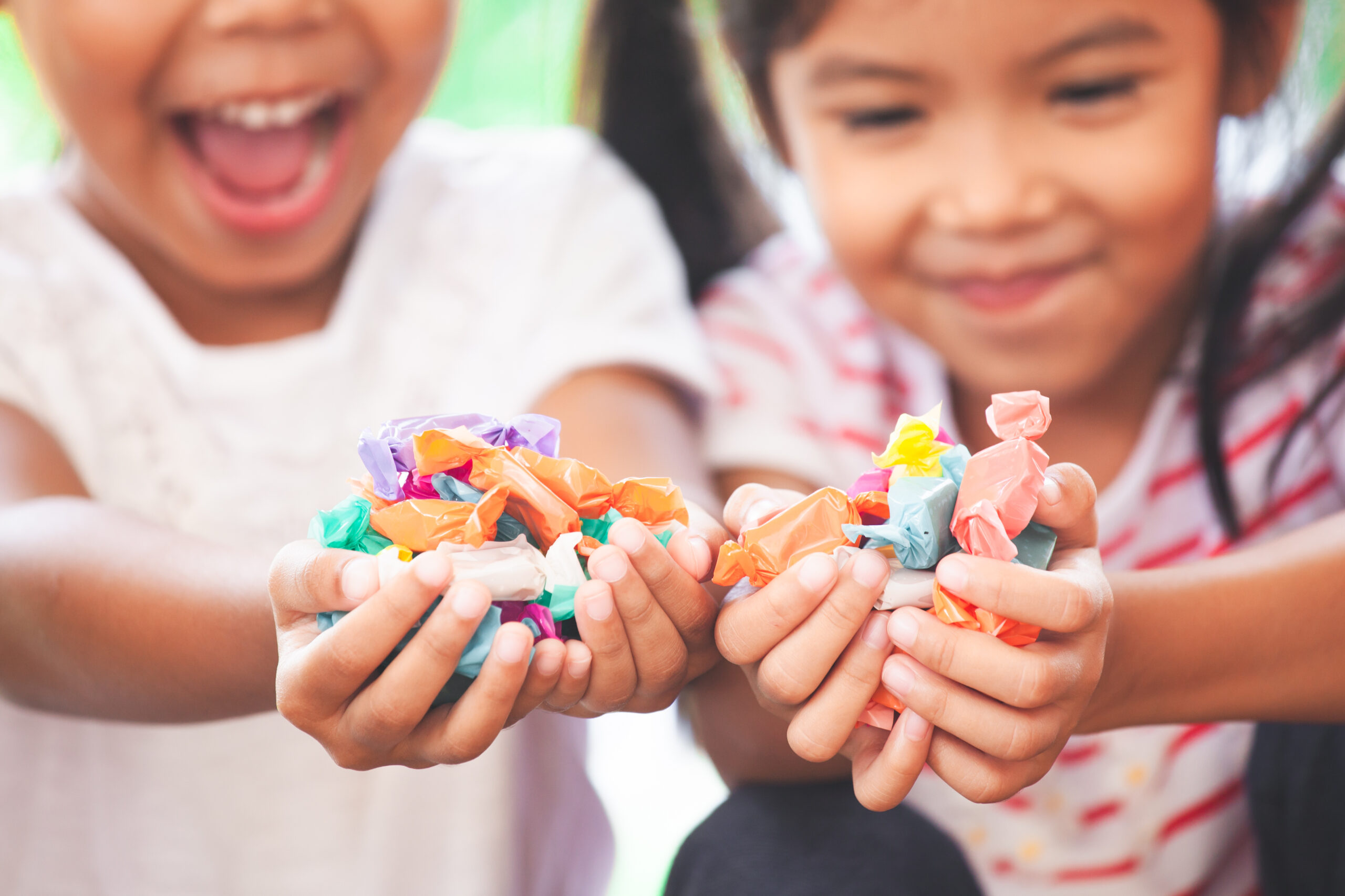 Zwei Kinder halten ihre Hände in die Kamera. Diese sind vollgefüllt mit verschiedenen bunten Zuckerln.