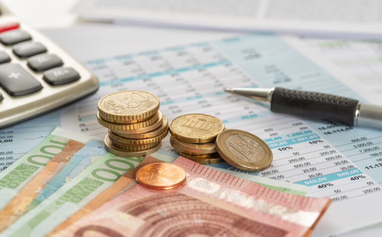 Münzen und Geldscheine liegen auf einem Ausdruck mit Zahlen.