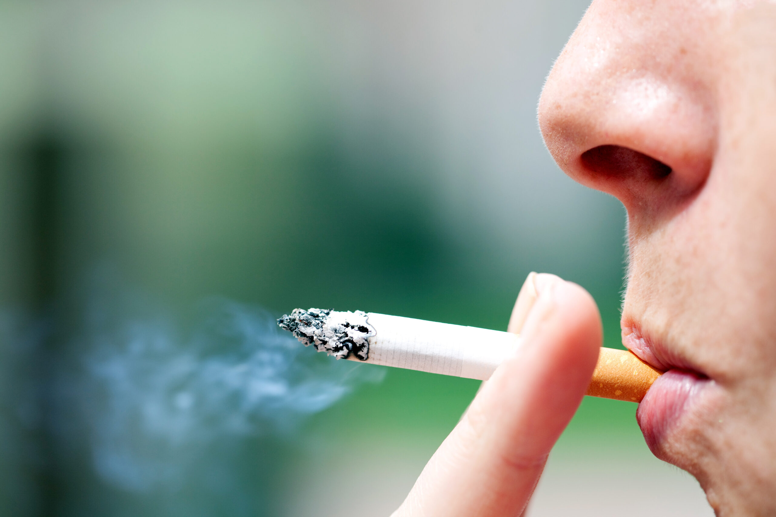 Person, von der nur der vorderste Gesichtsteil zusehen ist, hat eine Zigarette zwischen den Lippen und hält sie mit zwei Fingern.