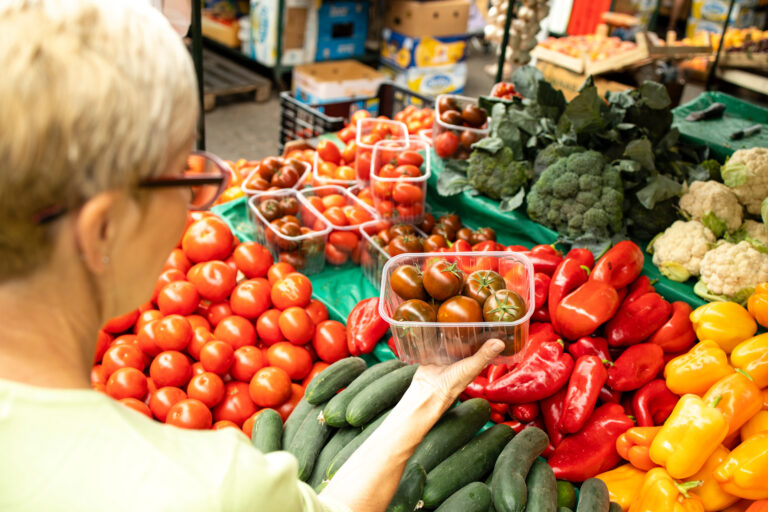 Frau steht am Gemüsestand und hält eine Tasse mit Tomaten in der Hand.