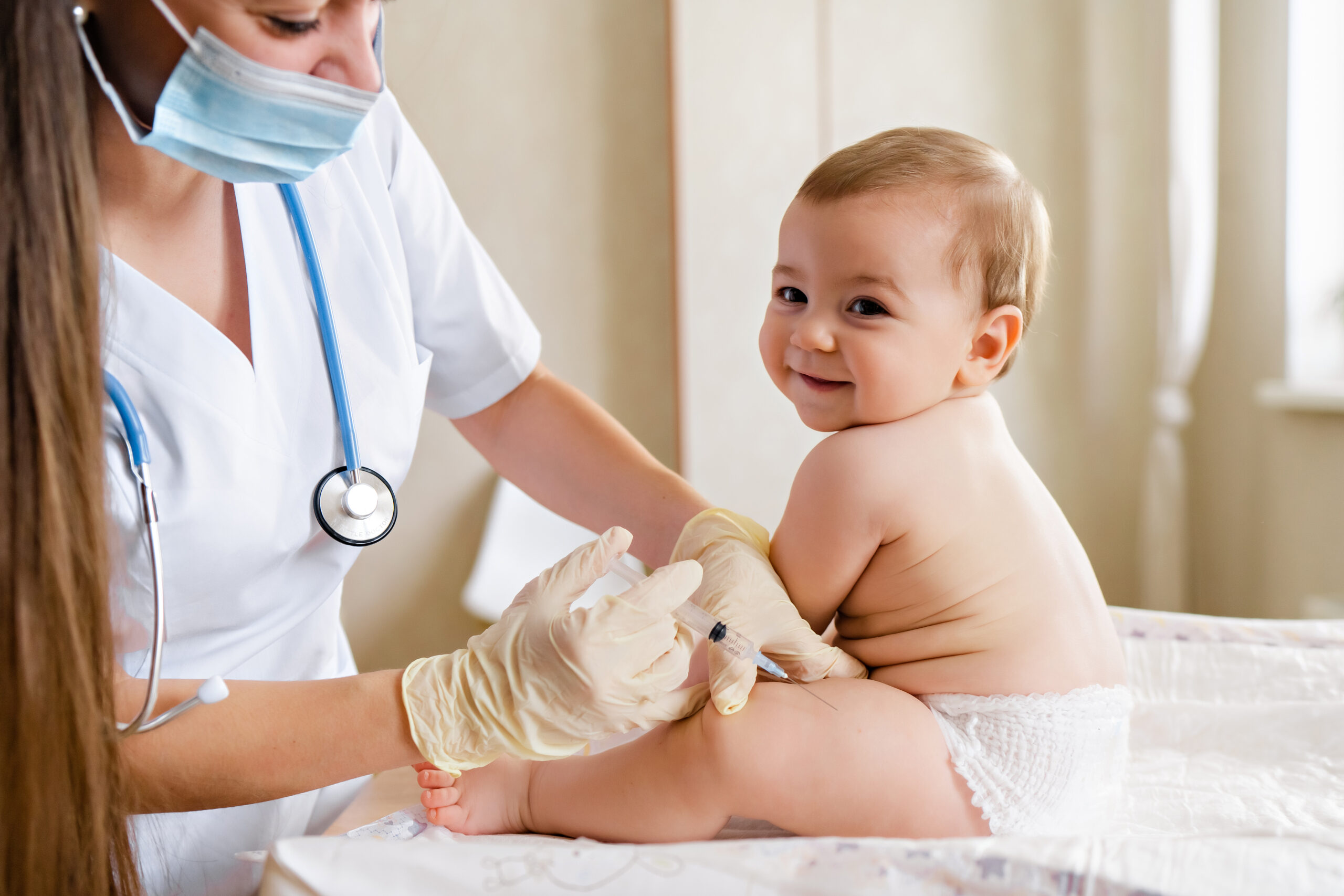 Baby wird von einer Ärztin in den Oberschenkel geimpft und lächelt dabei.