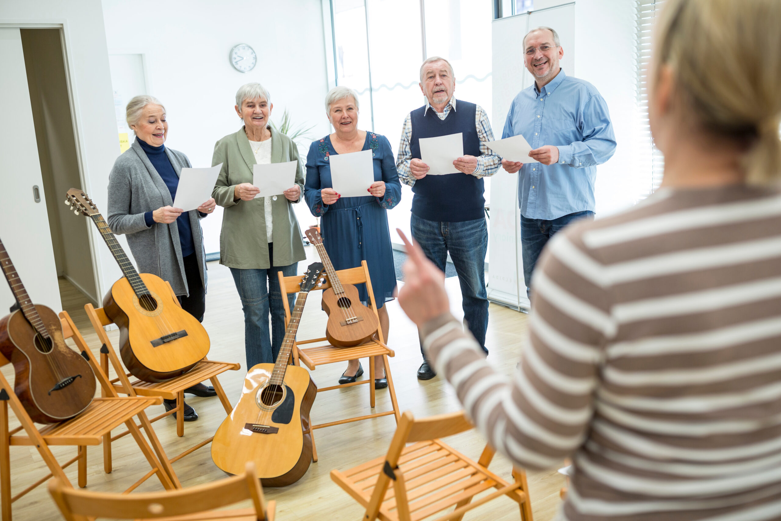 Gruppe älterer Personen singt mit Noten in der Hand. Daneben stehen Gitarren.