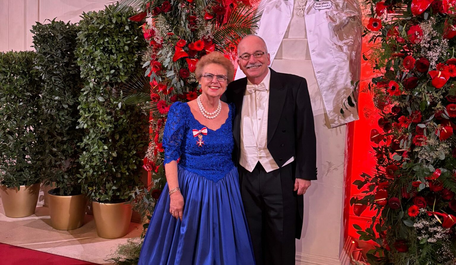 Christl Kören und ihr Gatte stehen in Ballkleidung vor der Büste von Kaiser Franz Josef.