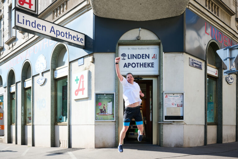 Mann springt vor der Apotheke und streckt eine Faust in die Höhe.