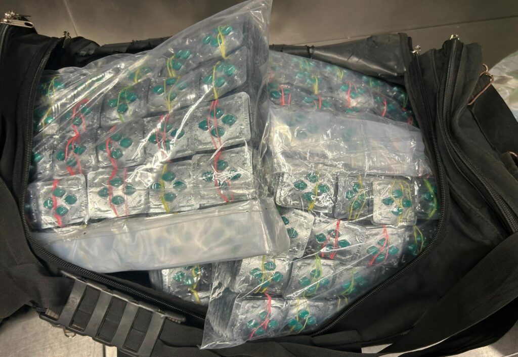 Eine schwarze geöffnete Reisetasche mit grünen Pillen im Reis angeordnet im Blister.