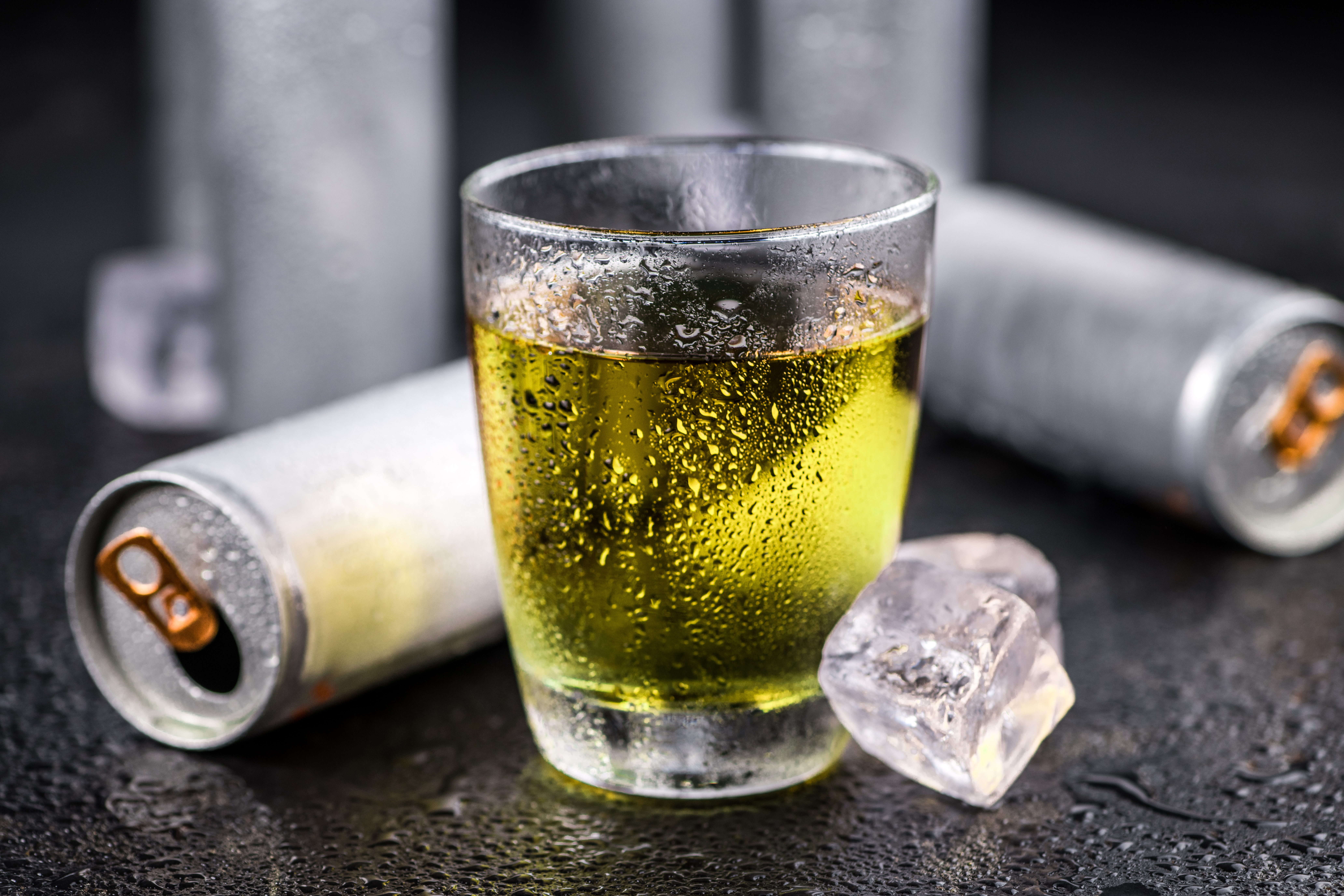 Zwei silberne Dosen liegen neben einem Glas mit gelblicher Flüssigkeit.