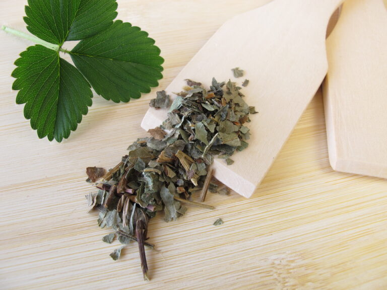 Ein Erdbeerblatt liegt neben einem Holzspartel der mit Tee beschüttet ist.