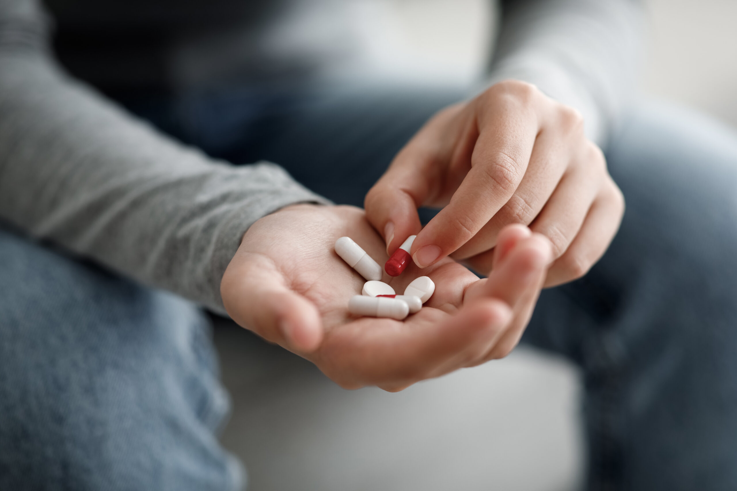 Mann, der in seiner Hand verschiedene Tabletten und eine rot-weiße Kapsel hält.