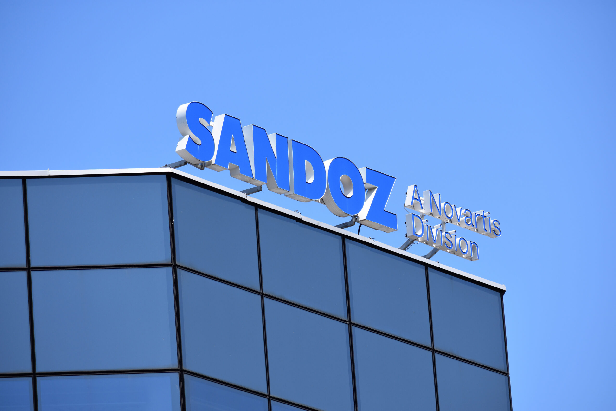 Ein Ausschnitt einer Häuserwand auf dem das Sandoz Logo in blau angebracht ist.