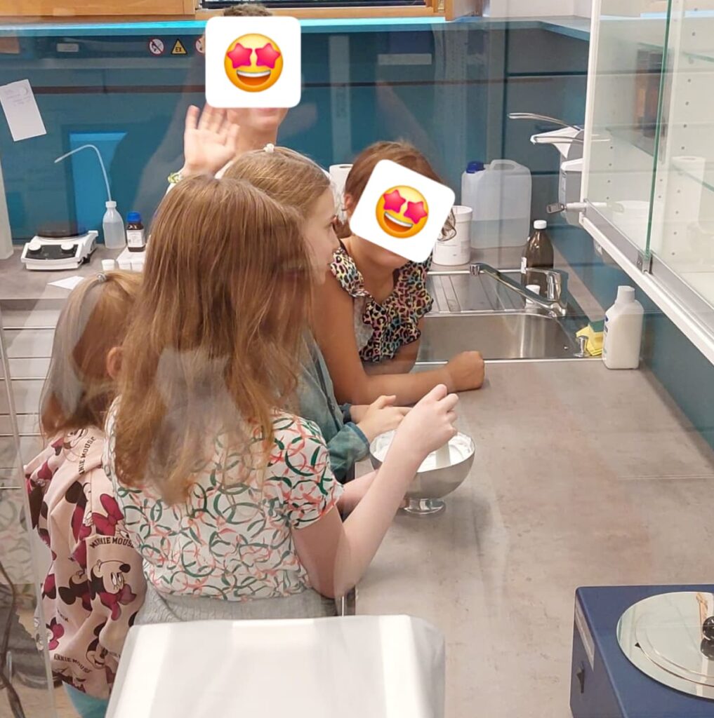 Man sieht eine Gruppe von Mädchen in der Rezeptur der Apotheke eine Salbe rühren. Eines von ihnen hält den Pistill und rührt in der Patene.