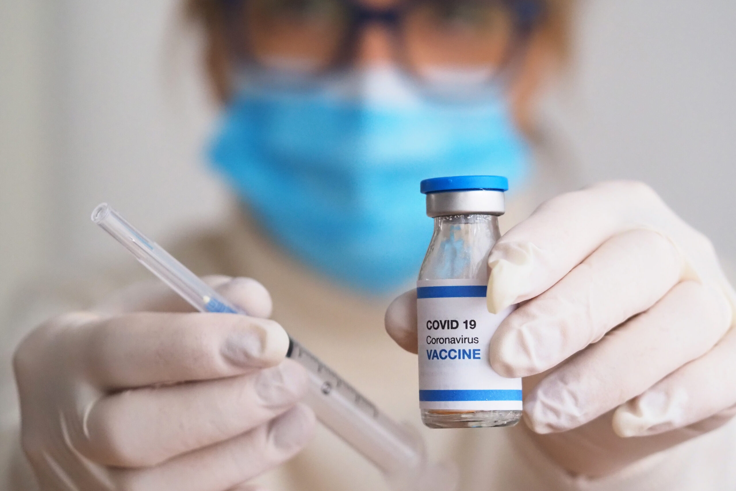 Symbolbild: Eine Frau hält eine Impfstoffflasche mit der Aufschrift "Covid-19 Vaccine" und eine Spritze hoch. Sie trägt Latexhandschuhe.