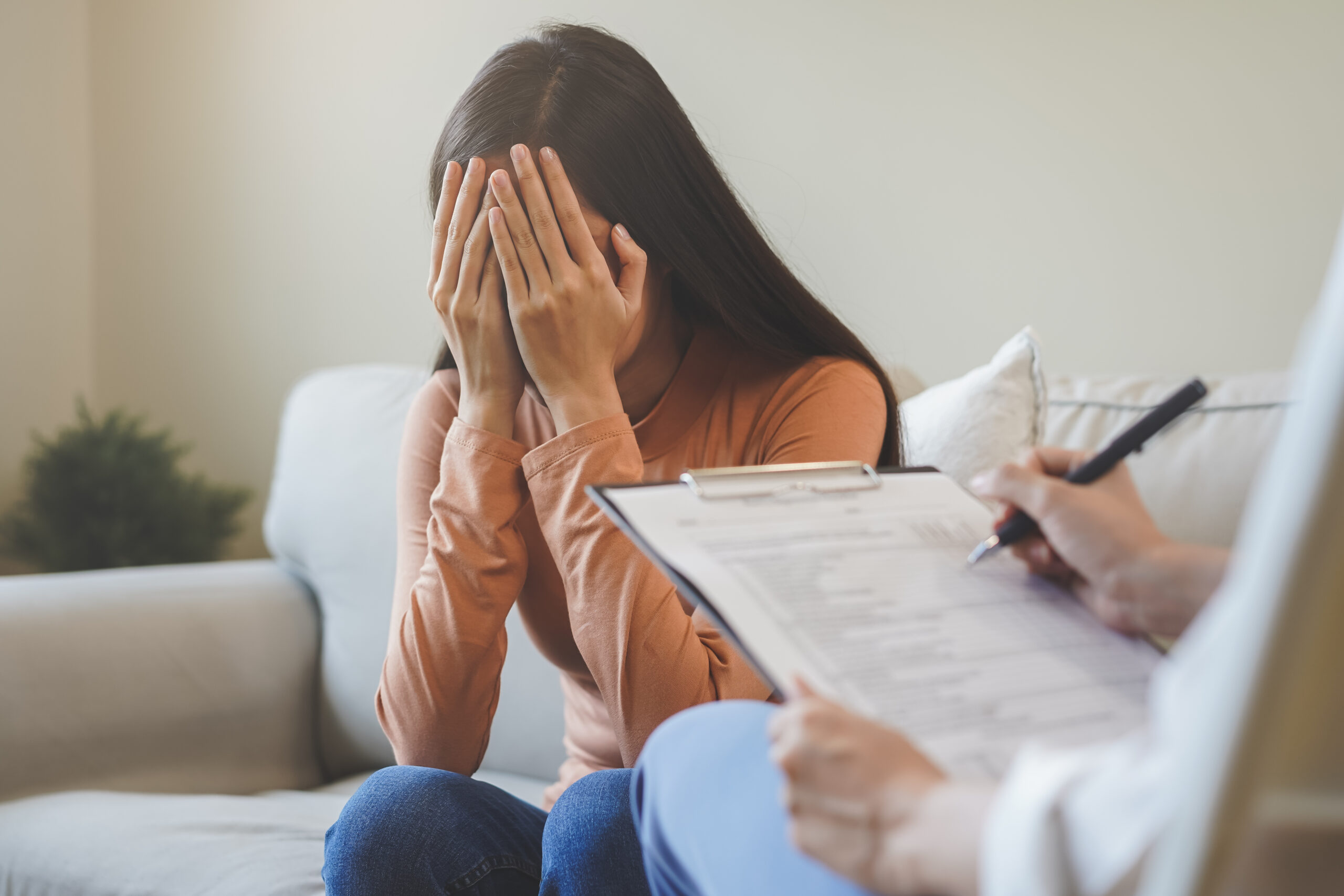 Symbolbild: Eine junge Frau hält sich die Arme vor das Gesicht. Sie ist in einer Therapiesitzung.