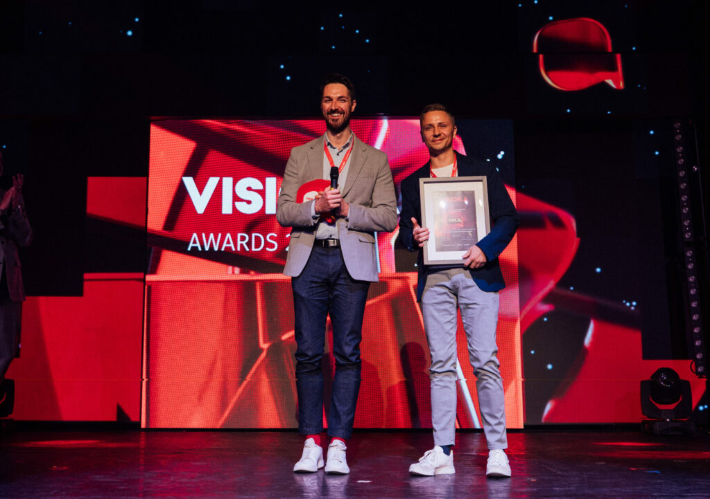 Apotheker Manuel Wendl und sein Lebensgefährte bei der Preisübergabe. Er hält den Award in seinen Händen und lacht.