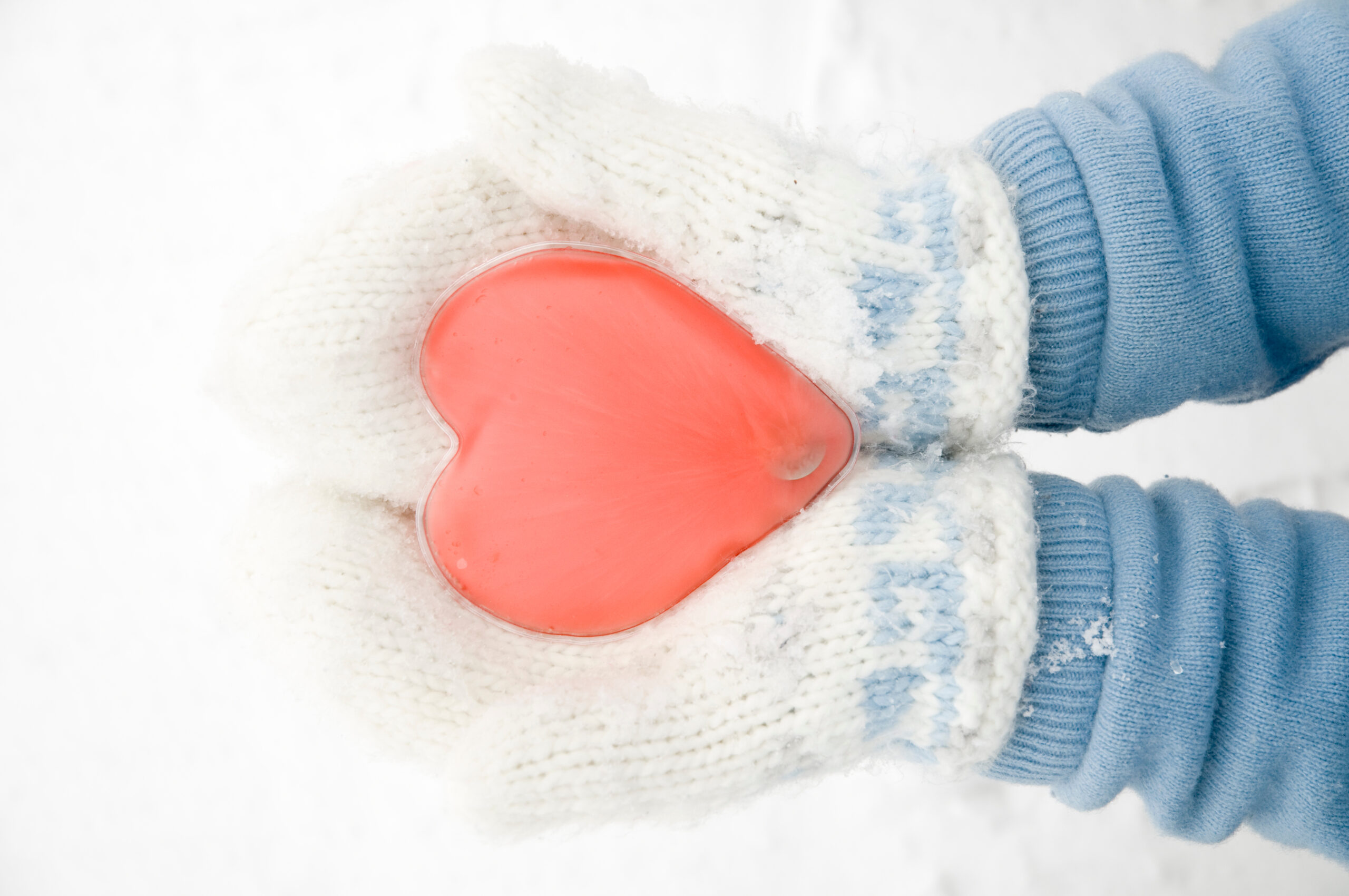 Symbolbild: Zwei Hände mit Handschuhen halten einen roten herzförmigen Handwärmer im Schnee.