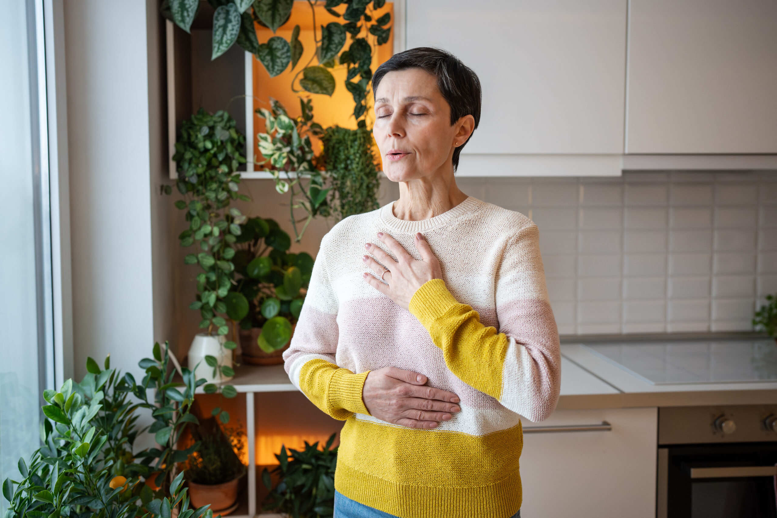 Symbolbild: Eine ältere Damen in Strickpullover atmet tief durch. Sie hält eine Hand auf ihren Bauch und die Andere auf ihre Brust.