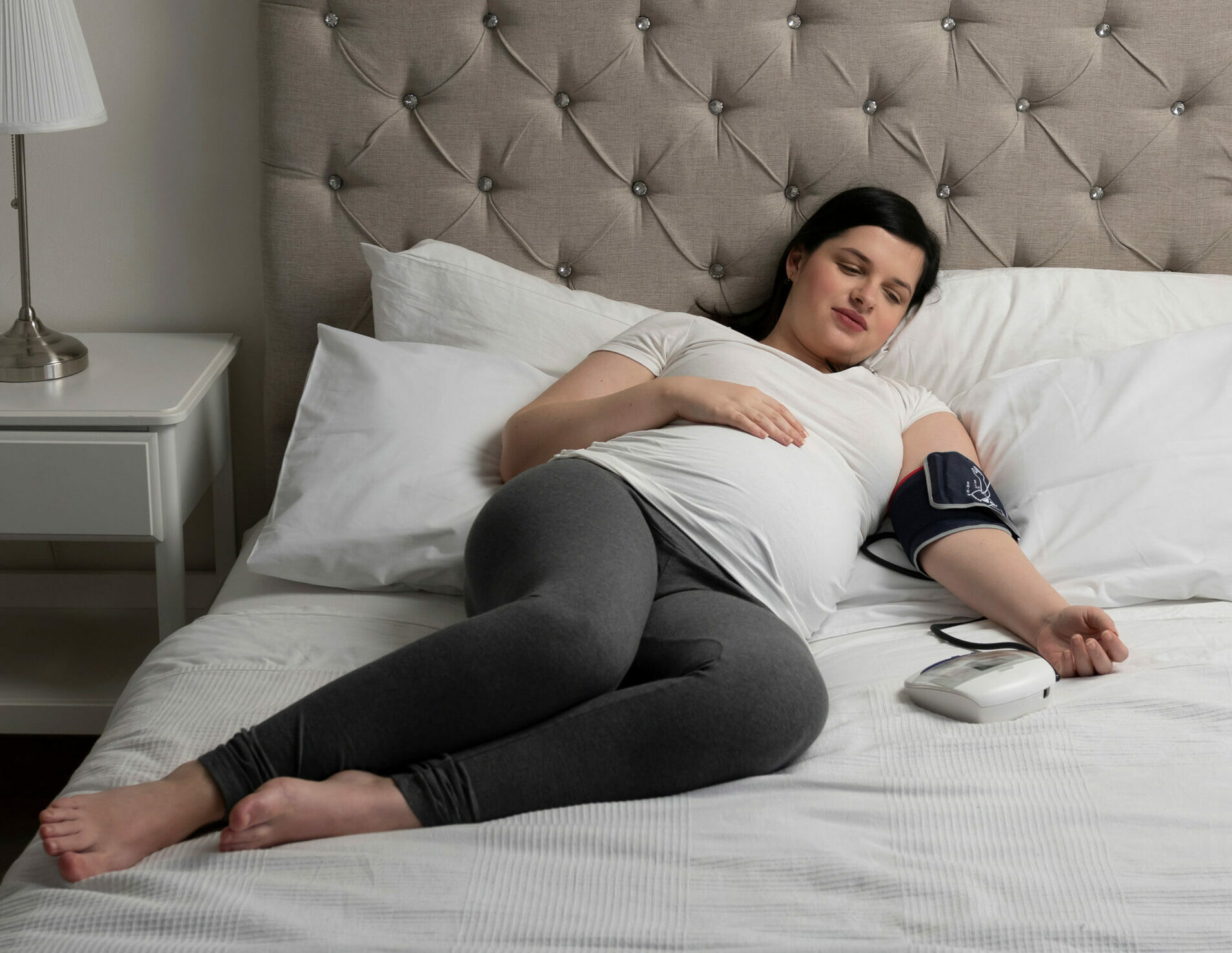 Symbolbild: Eine Schwangere liegt auf den Bett und misst sich den Blutdruck. Ihr Gesicht ist verzerrt.