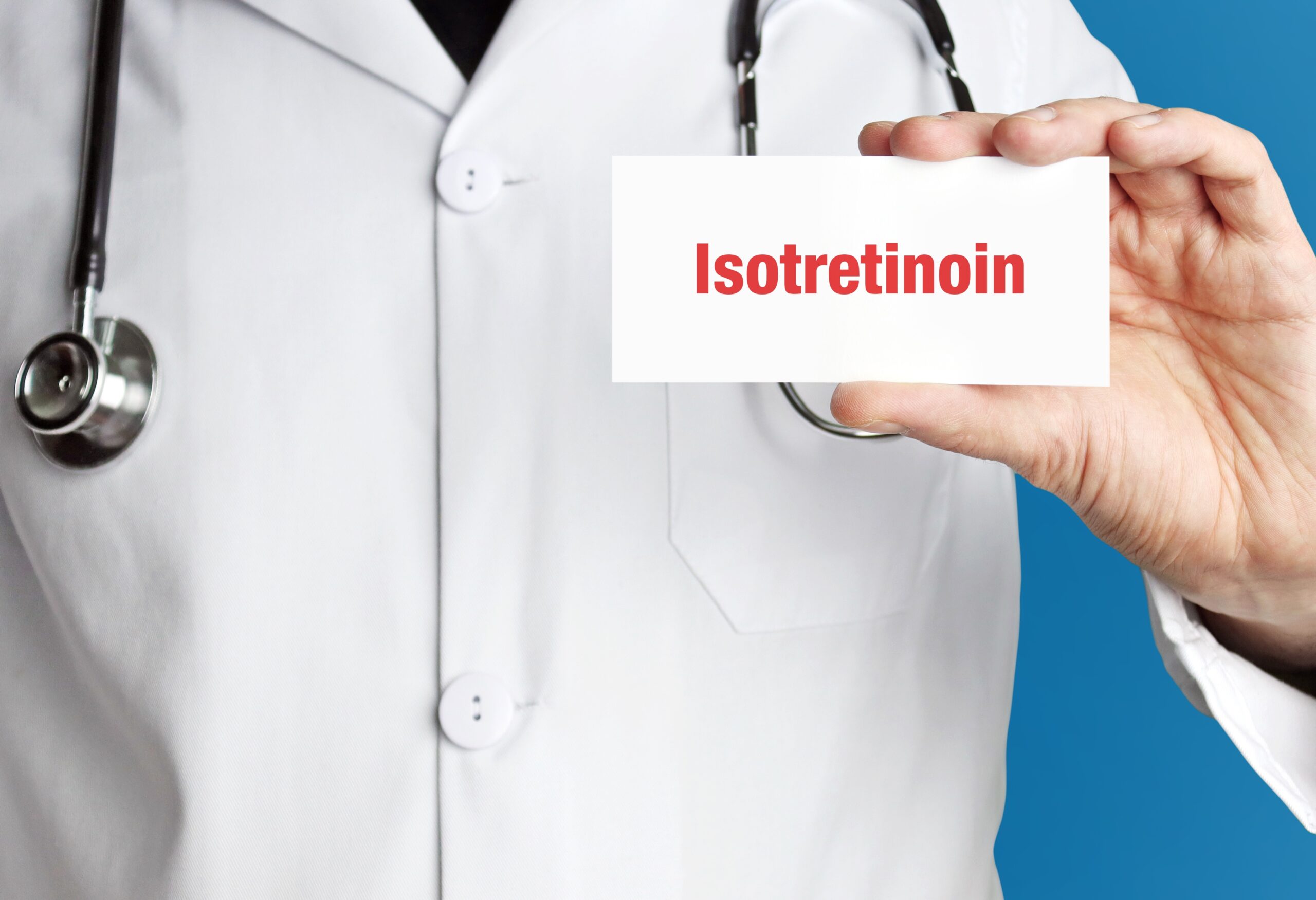 Symbolbild: Ein Mann im weißen Mantel und Stethoskop hält ein Kärtchen mit der Aufschrift "Isotretinoin".
