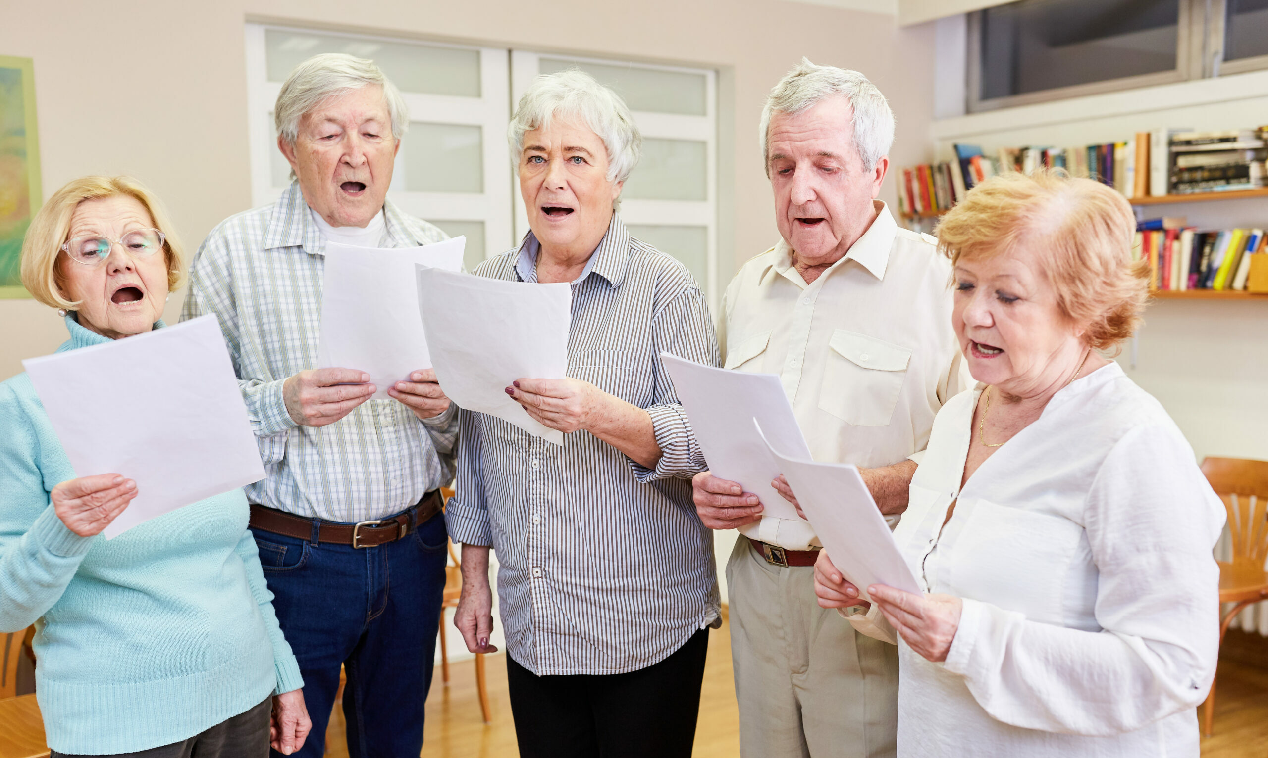 Symbolbild: eine Gruppe von Senioren und Seniorinnen singt gemeinsam. Sie halten ein Papier in der Hand und lesen die Noten ab.