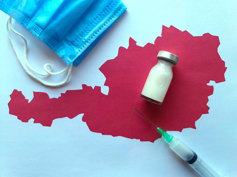 Symbolbild: Medizinflasche, Maske und Spritze auf einem Blatt Papier mit einer Karte von Österreich.