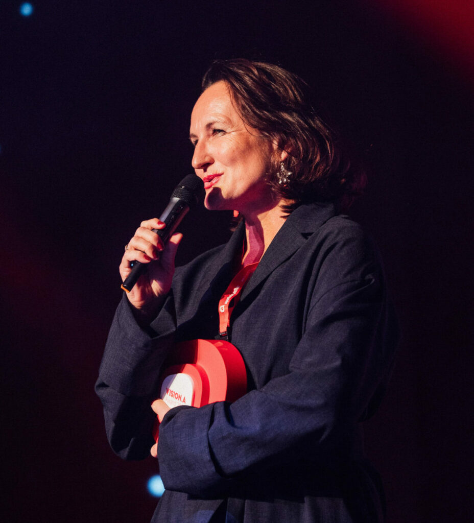 Gudrun Kreutzer hält ihren Award und spricht ins Mikrophon. Sie trägt ein blaues Kleid.
