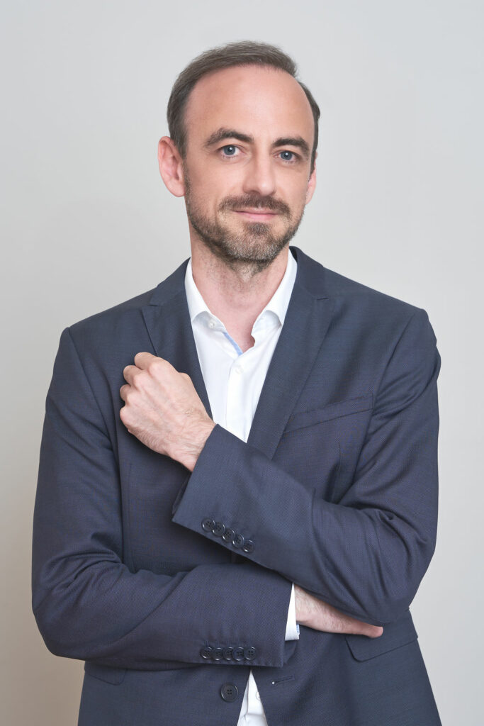 Markus Feldgrill trägt einen dunkelblauen Anzug und hat die Arme verschränkt-