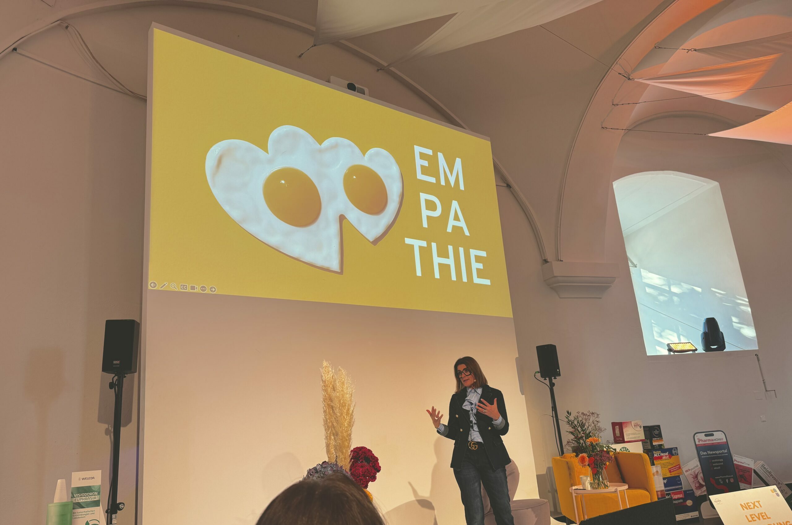 Sabine Hübner auf der Bühne der P.Tage. Hinter ihr ist eine Präsentation mit zwei herzförmigen Spiegeleiern und dem Wort "Empathie".