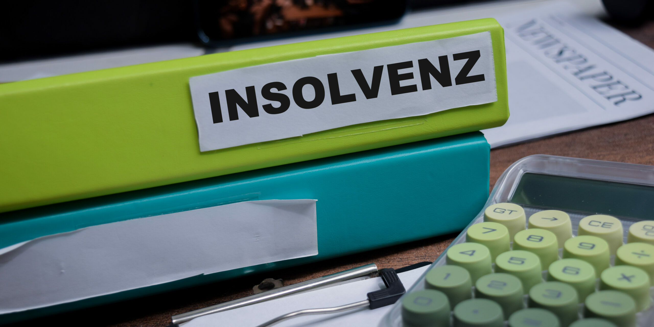 Symbolbild: Auf einem Tisch Ligen zwei Aktenordner. Auf einem Steht "Insolvenz", daneben liegt ein grüner Taschenrechner.
