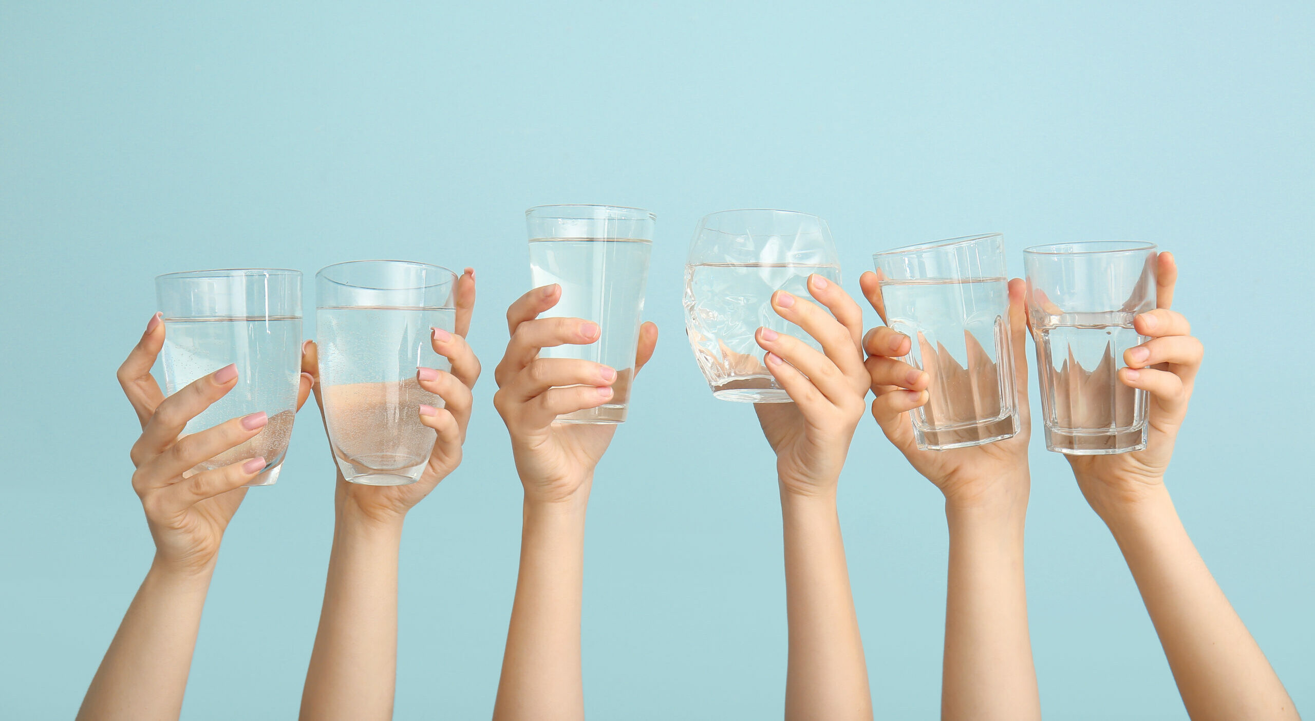 Symbolbild: Weiblichen Hände halten verschiedene Trinkgläser mit Wasser in die Höhe.