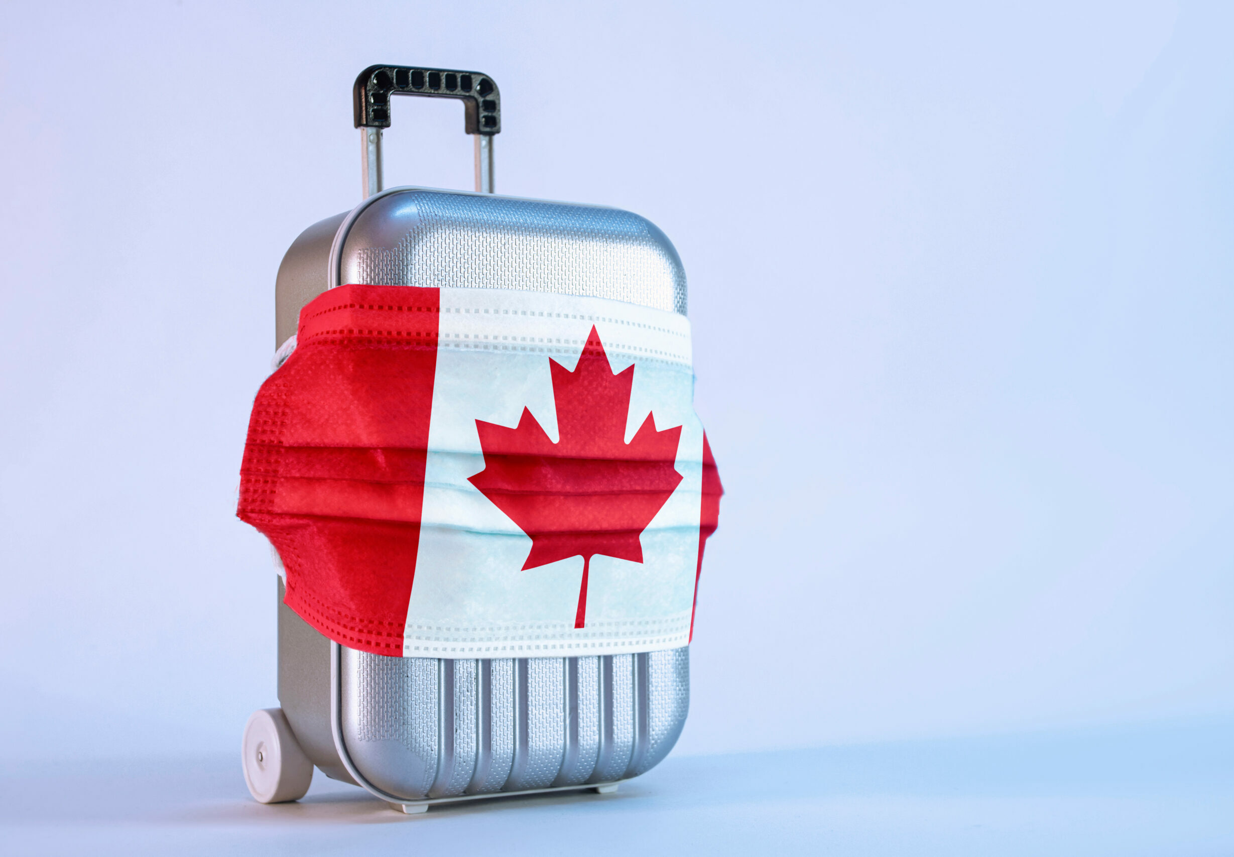 Symbolbild: Ein Koffer ist mit einem Mund-nasenschutz umwickelt. Er trägt die Kanadische Flagge.