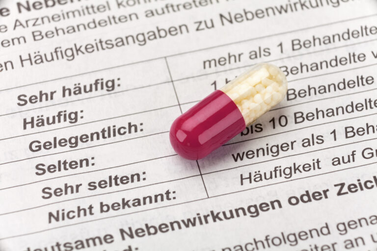 Symbolbild: Eine Weiß-rote Kapsel liegt auf einem beipacktest. Man sieht die Nebenwirkungen von sehr häufig bis nicht bekannt aufgelistet.