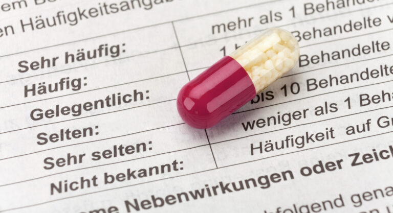 Symbolbild: Eine Weiß-rote Kapsel liegt auf einem beipacktest. Man sieht die Nebenwirkungen von sehr häufig bis nicht bekannt aufgelistet.