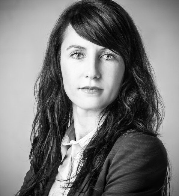 kristin Mann ista uf einem schwarz-weiß Foto zu sehen. Sie trägt einen Blazer und eine weiße Bluse.