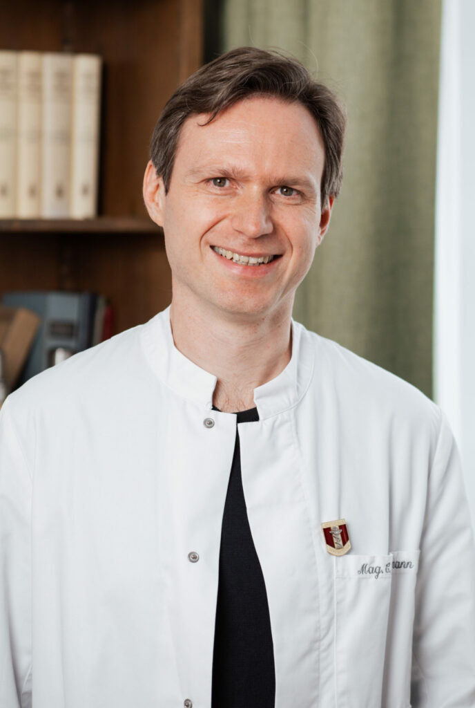 Apotheker Clemens Feldmann ist im weißen Mantel vor einem Bücherregal zu sehen.