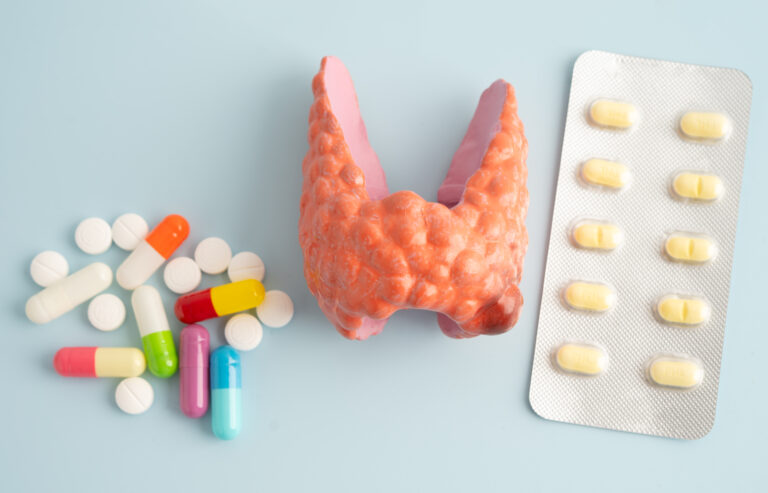 Symbolbild: Ein Modell einer Schilddrüse liegt neben einem Haufen Kapseln und Tabletten, daneben ein Blisterstreifen.